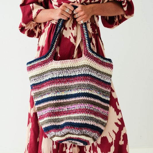 Person holding a striped handbag wearing a patterned dress on a white background