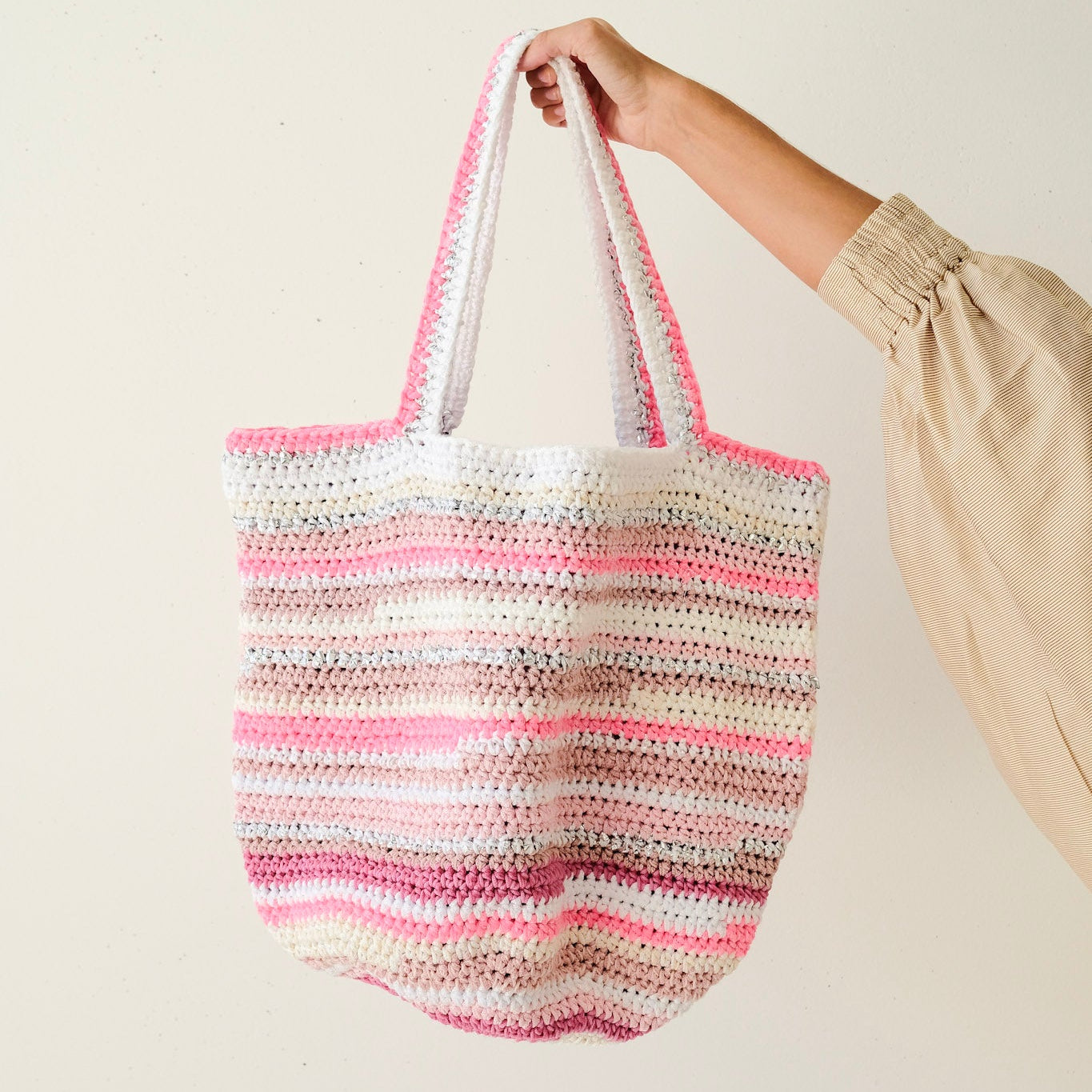 Hand holding a striped crochet bag against a plain background