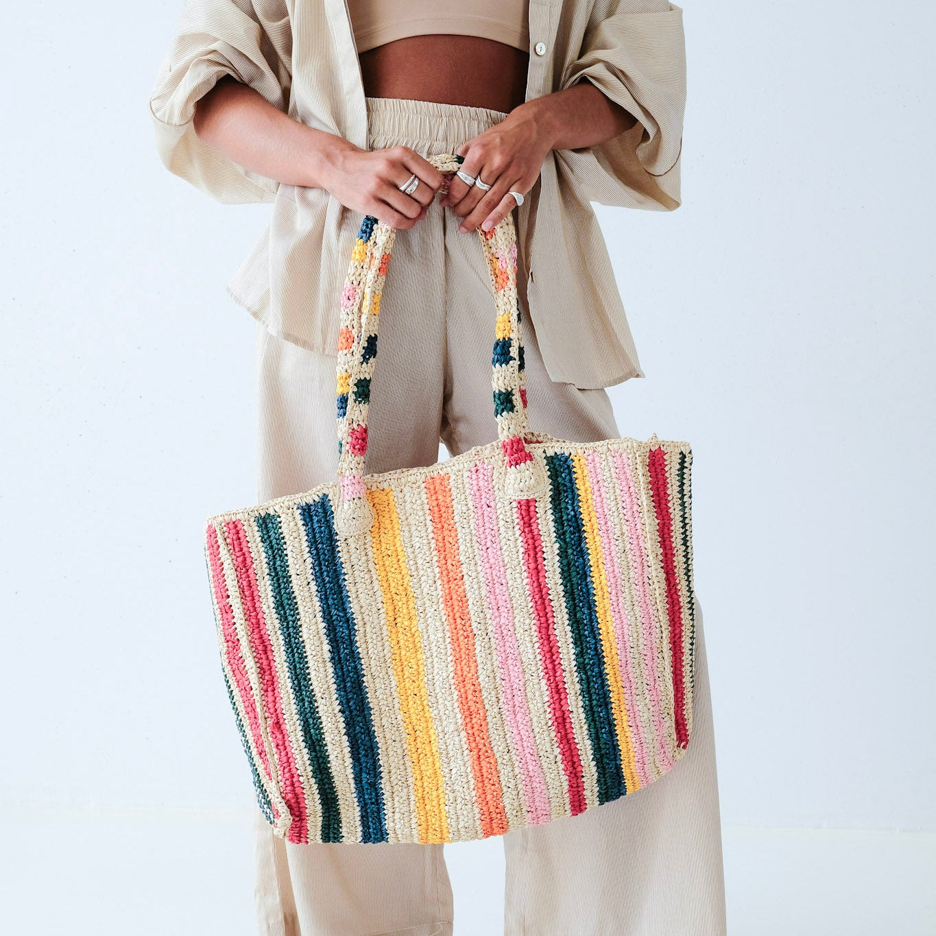 Person holding a colorful striped woven bag against a white background