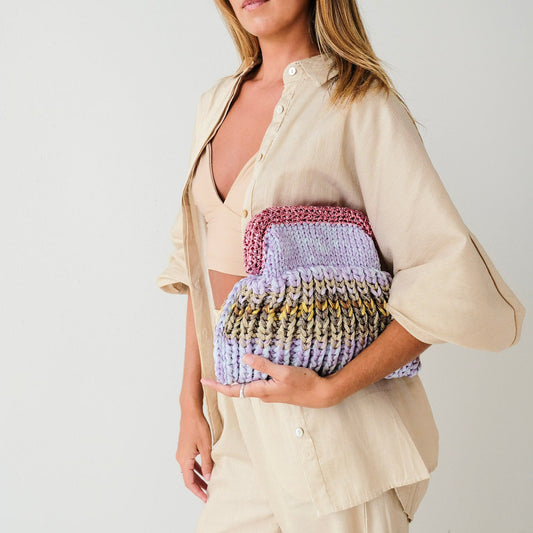 Woman wearing a beige shirt over a colorful knit top with beige pants against a white background