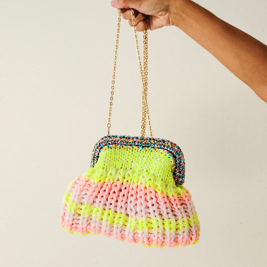 Hand holding a colorful knitted handbag with a chain strap against a plain background