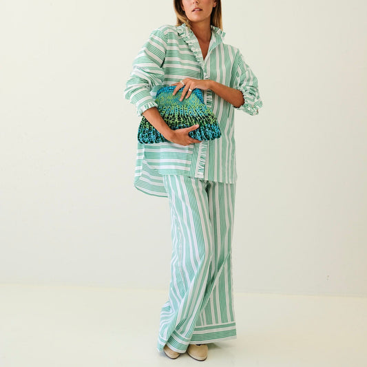 Woman wearing a striped outfit holding a clutch against a plain background