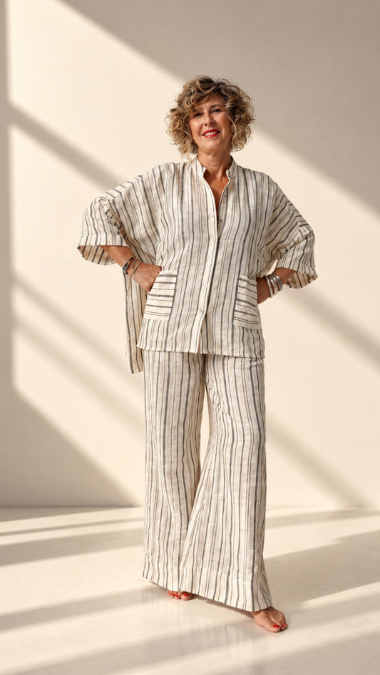 A woman modeling a matching two-piece lounge set with vertical stripes, standing in a brightly lit studio with diagonal shadows.