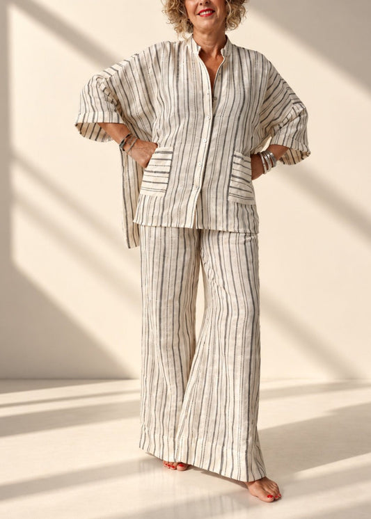 A woman modeling a matching two-piece lounge set with vertical stripes, standing in a brightly lit studio with diagonal shadows.