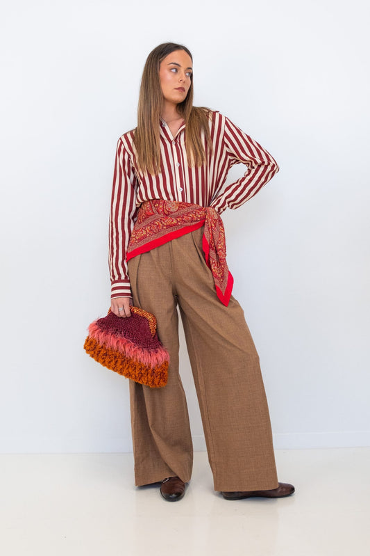 Model wearing Chocolate Prince of Wales wide-leg pants with a red-and-white striped shirt, red scarf, and textured handbag.