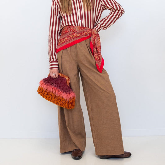 Model wearing Chocolate Prince of Wales wide-leg pants with a red-and-white striped shirt, red scarf, and textured handbag.