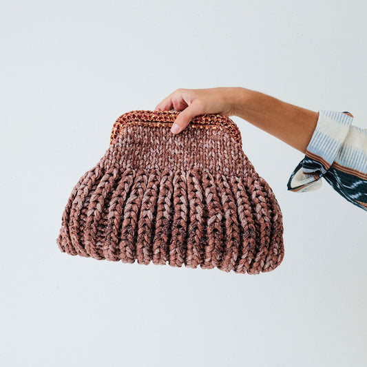 Hand holding a brown woven clutch bag against a white background