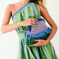 Woman wearing a green and purple striped dress holding a colorful clutch against a white background