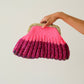 Hand holding a pink knitted clutch bag with a gold frame against a plain background