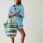 Woman holding a colorful striped bag wearing a blue patterned dress on a plain background