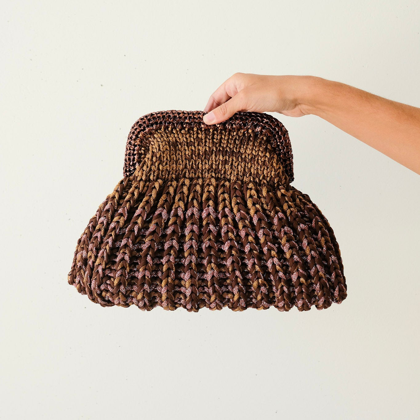 Hand holding a textured brown handbag against a light background