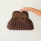 Hand holding a textured brown handbag against a light background