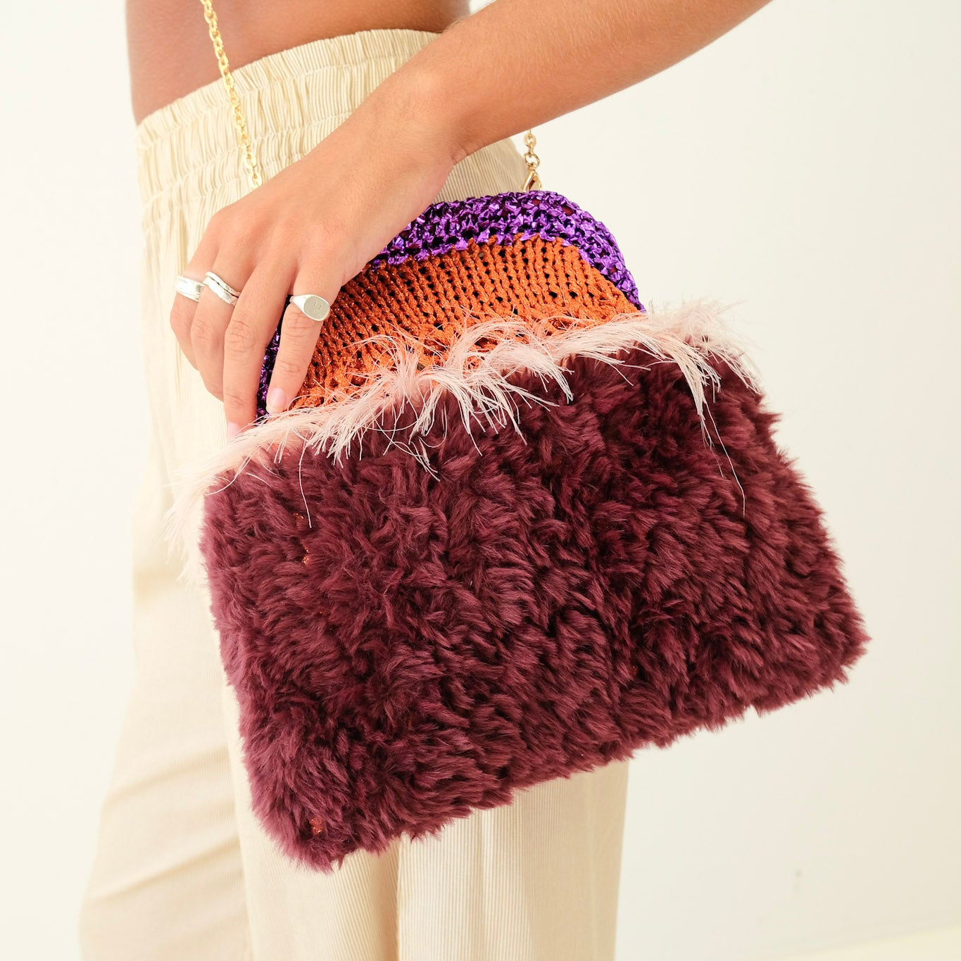 Person holding a colorful clutch with feather detail against a neutral background