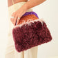 Person holding a colorful clutch with feather detail against a neutral background
