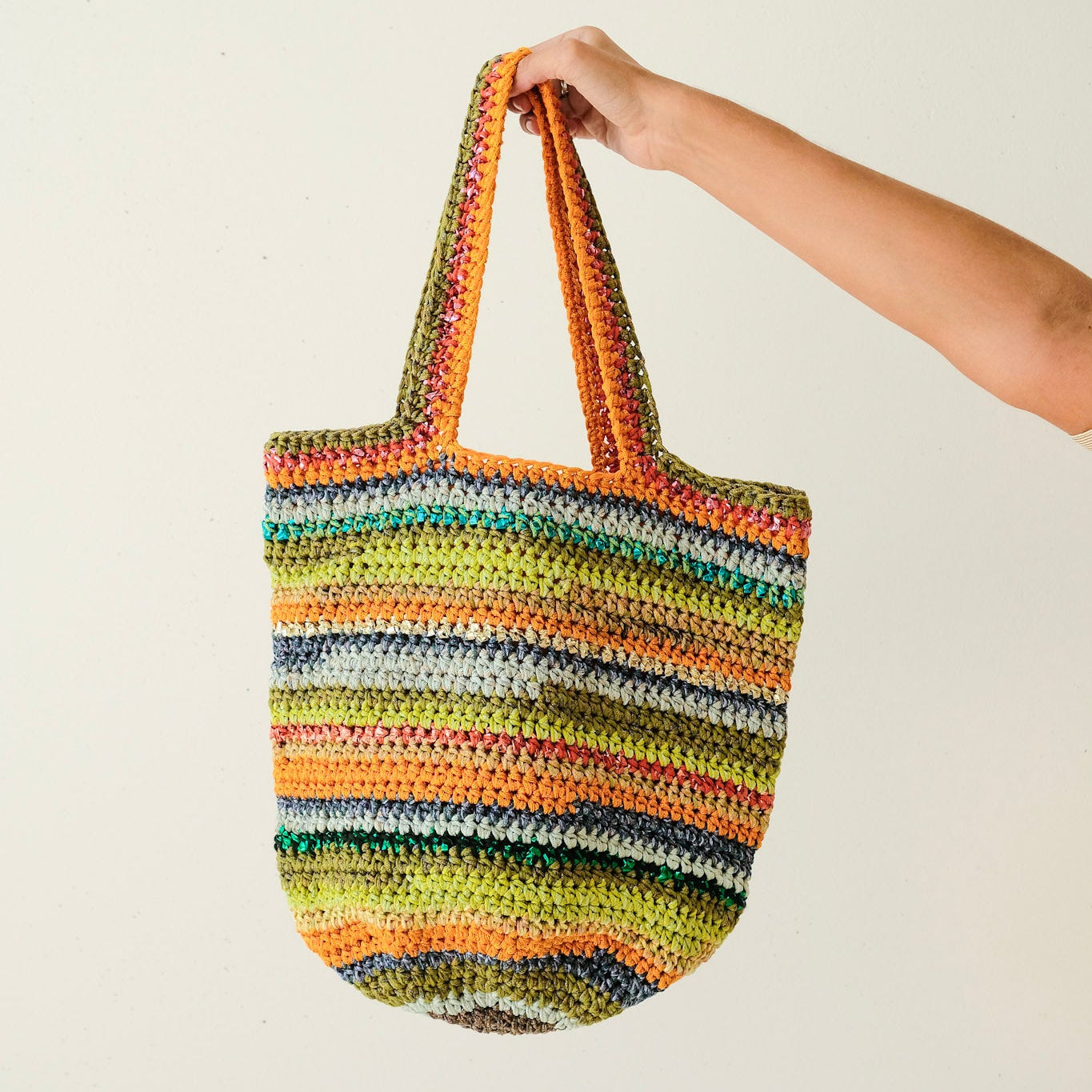 Colorful striped crochet bag held by a person against a plain background