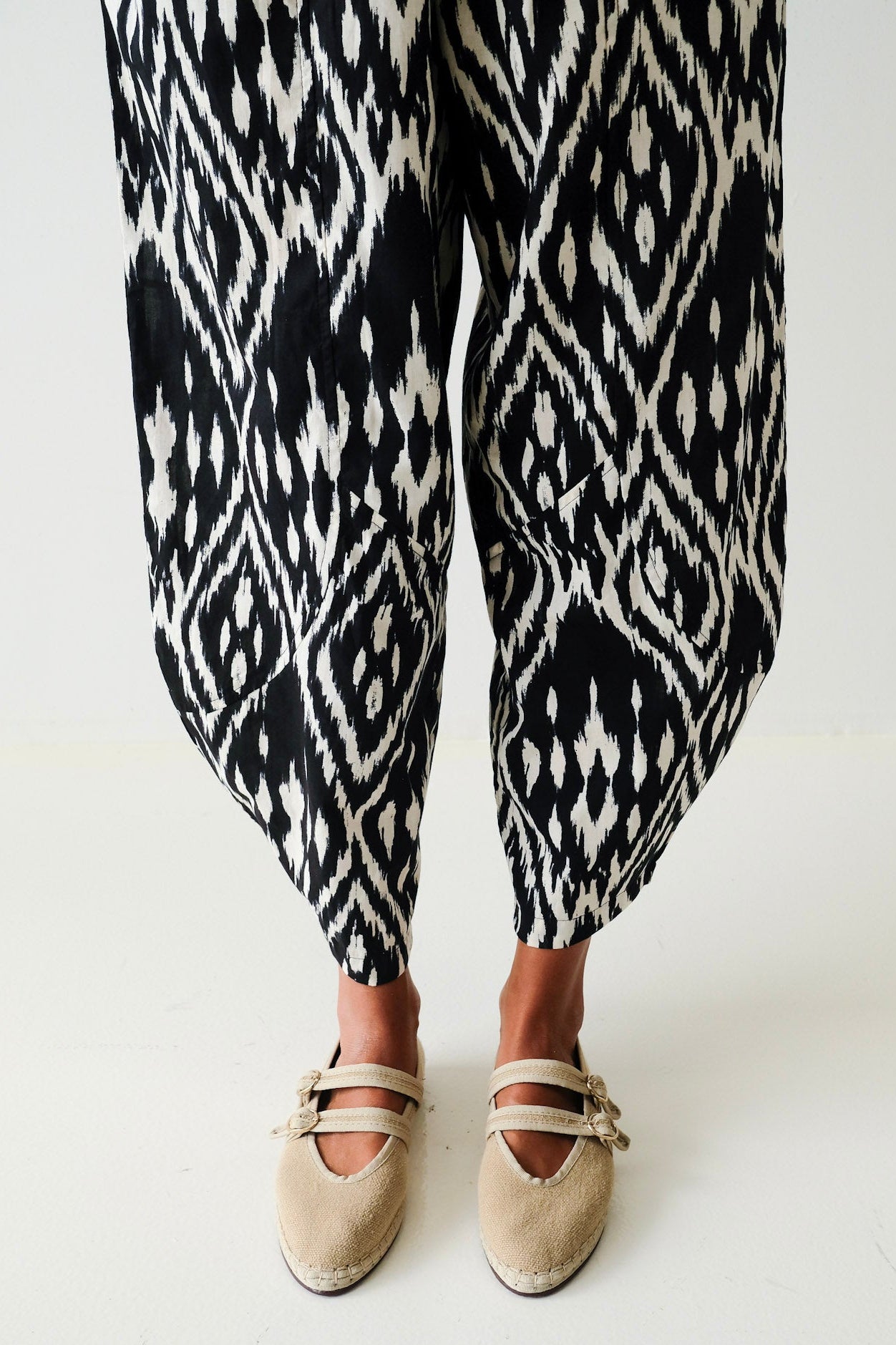 Person wearing black and white patterned pants with beige shoes on a white background