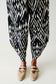 Person wearing black and white patterned pants with beige shoes on a white background