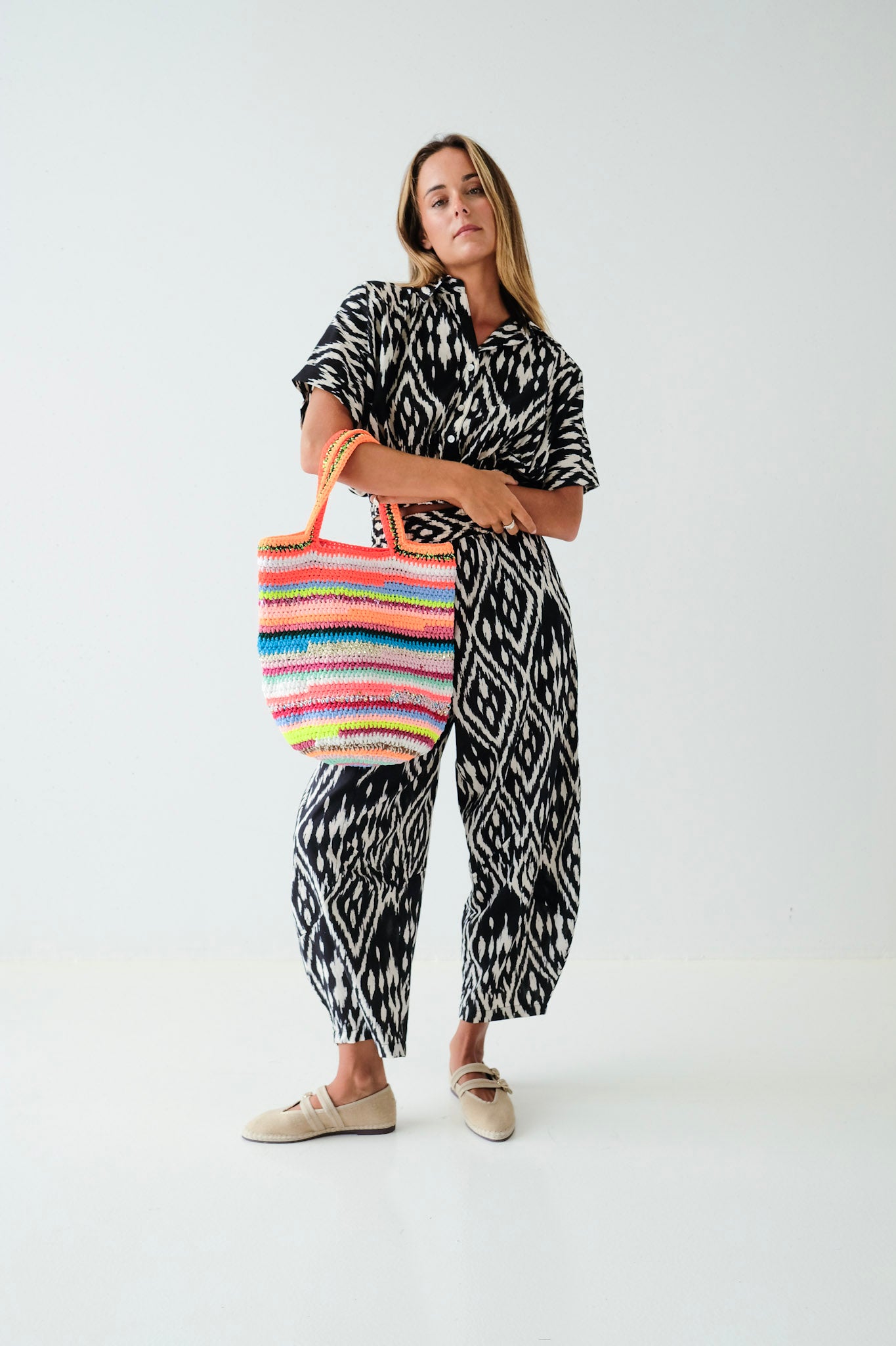 Woman holding a colorful striped bag wearing a black and white patterned outfit on a white background