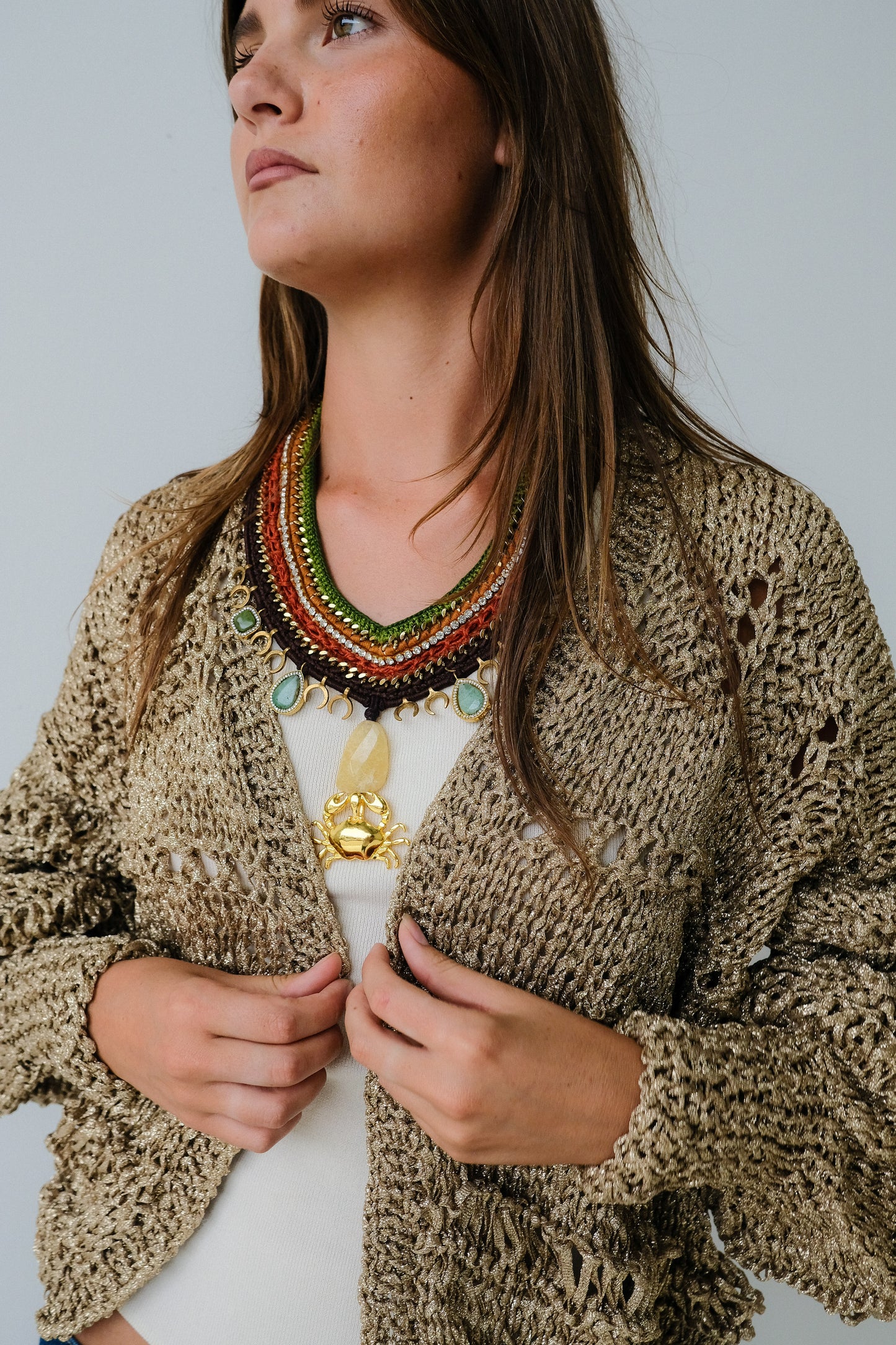 Woman wearing a patterned cardigan and colorful necklace against a plain background