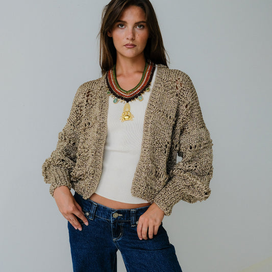 Woman wearing a beige cardigan, white top, and blue jeans against a plain background