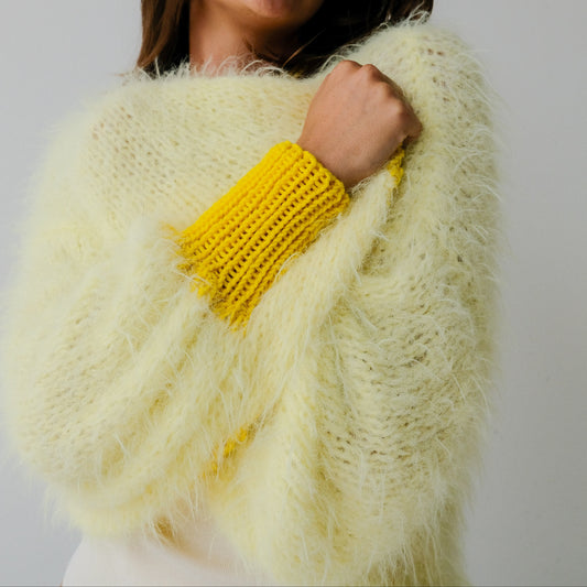 Woman wearing a light yellow knitted sweater with yellow cuffs against a plain background