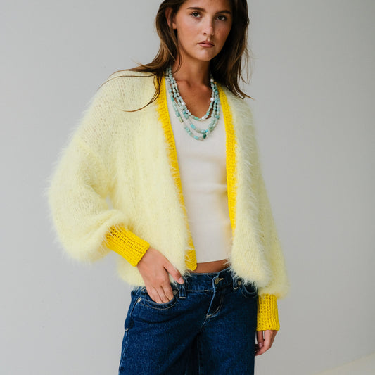 Woman wearing a light yellow cardigan over a white top and blue jeans on a plain background
