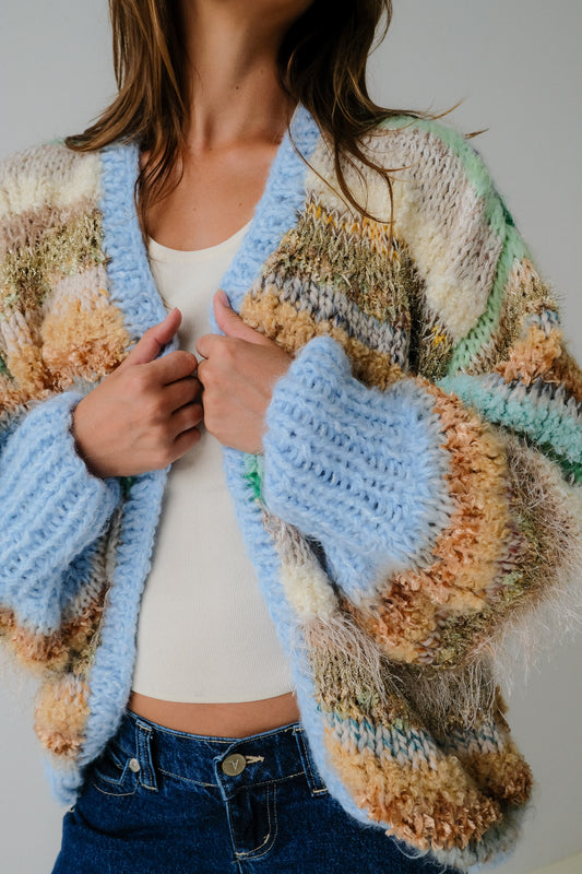 Person wearing a colorful knitted cardigan with a neutral background