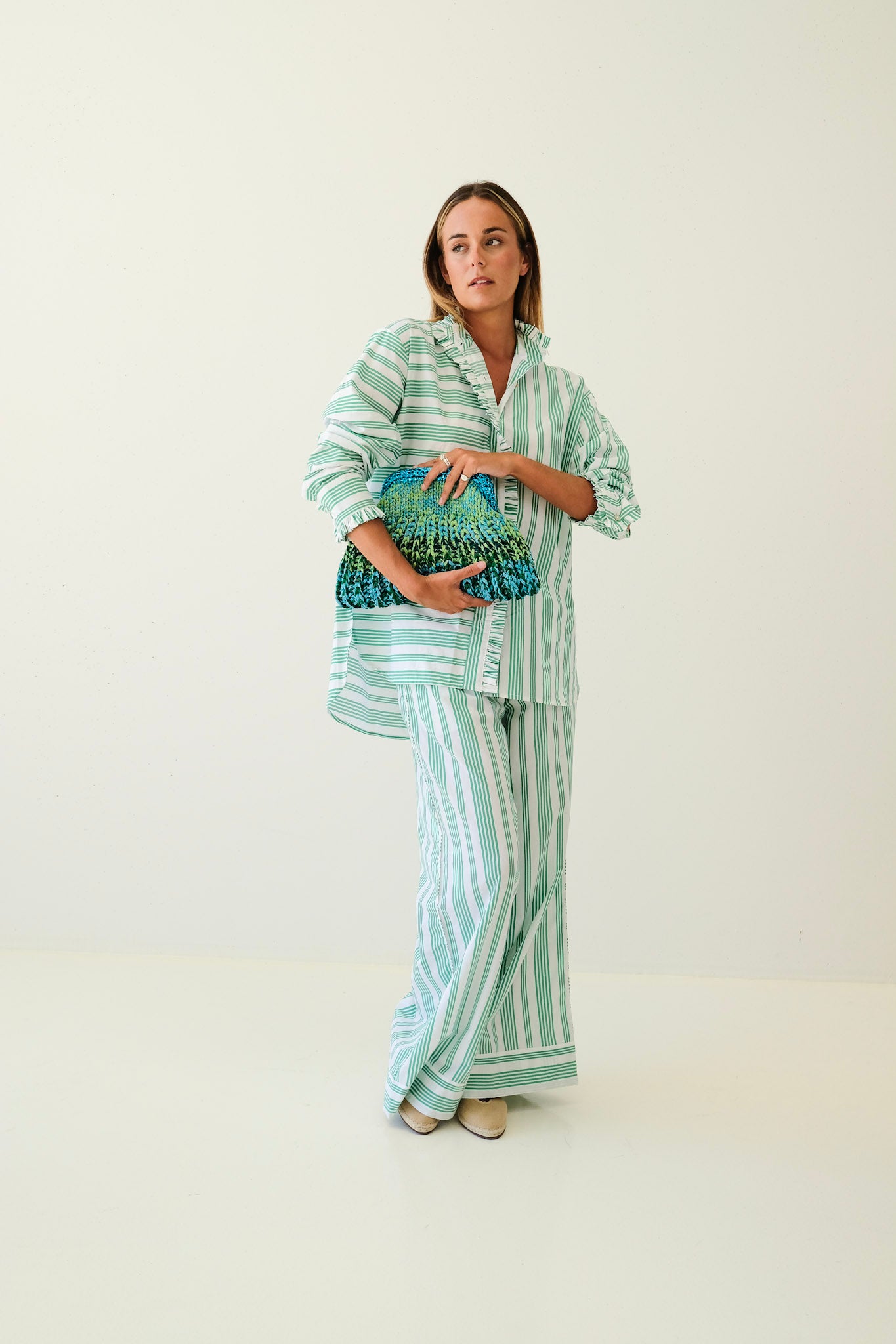 Woman wearing a striped outfit holding a clutch against a plain background