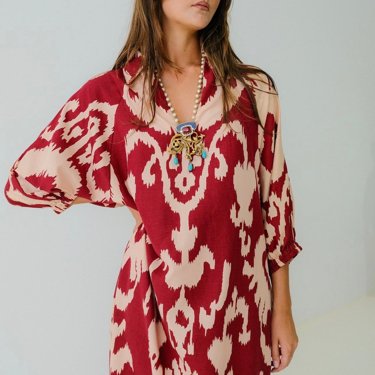 Woman wearing a red and white patterned dress with a pearl necklace against a white background