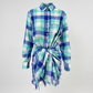 A long-sleeve plaid shirt dress in shades of blue, green, and white, featuring a button-down front, chest pocket, and a self-tie belt at the waist.