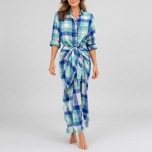 A woman modeling a blue, green, and white plaid wrap dress with a tie waist and fringed hem, standing against a plain white background.