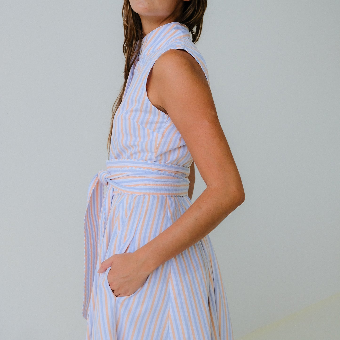 Woman wearing a sleeveless, striped dress against a plain background