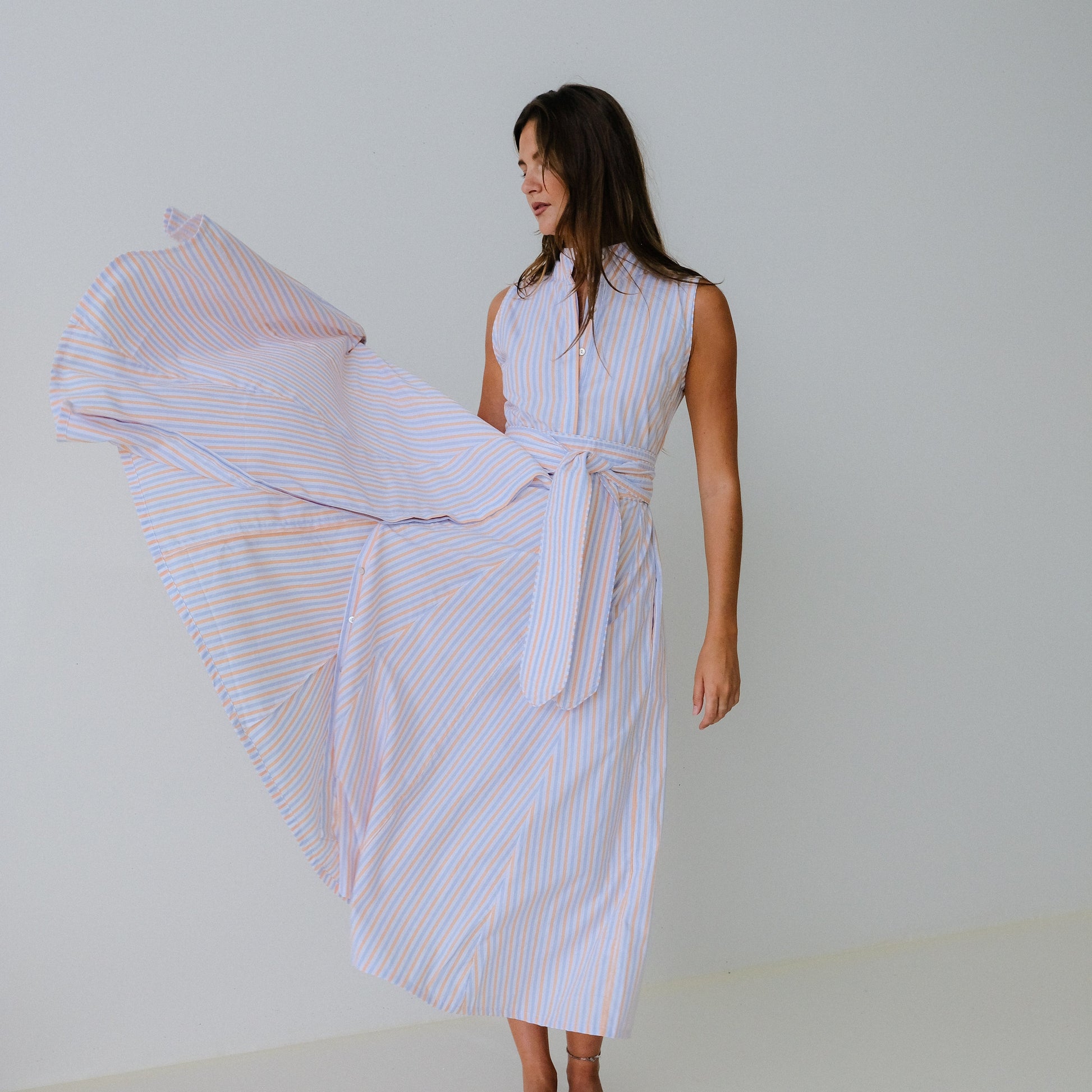 Woman wearing a white sleeveless dress with a flowing fabric against a plain background