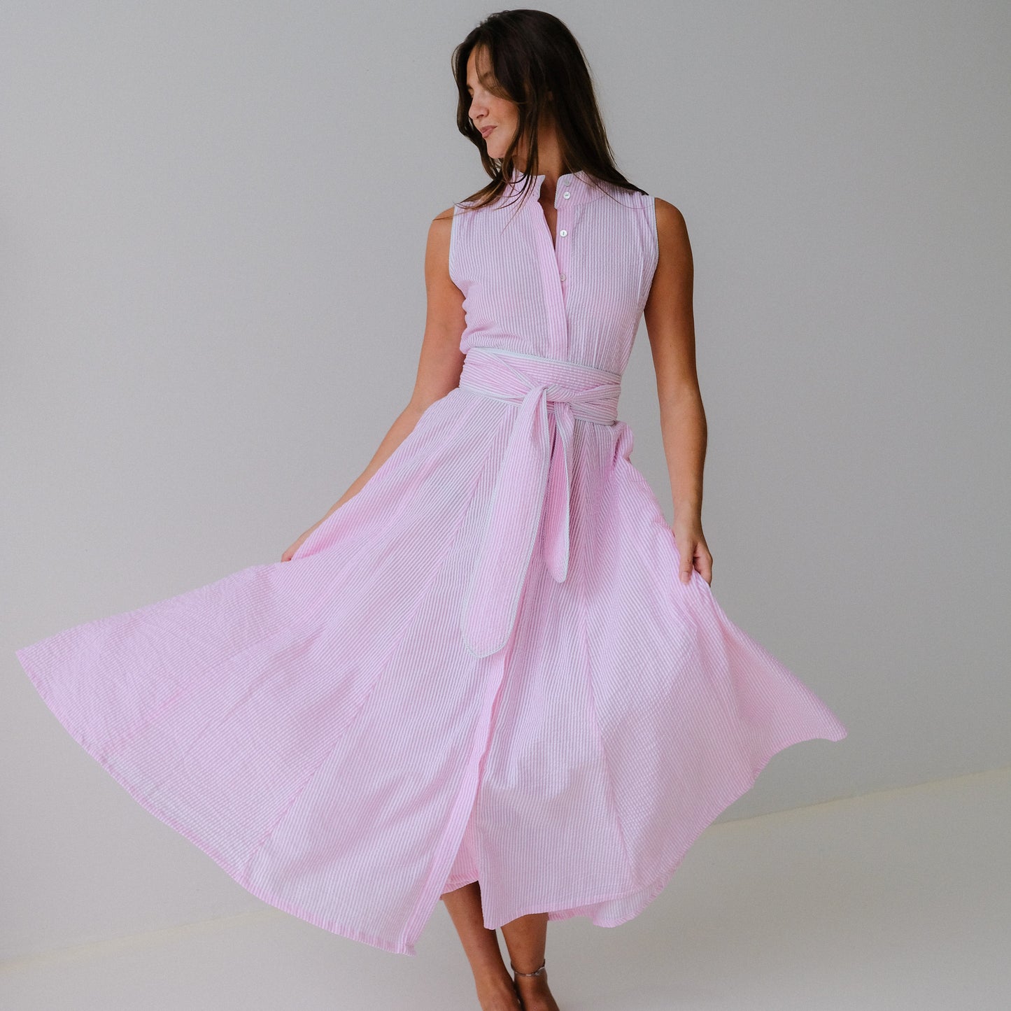 Woman wearing a light pink sleeveless dress with a belt against a plain background