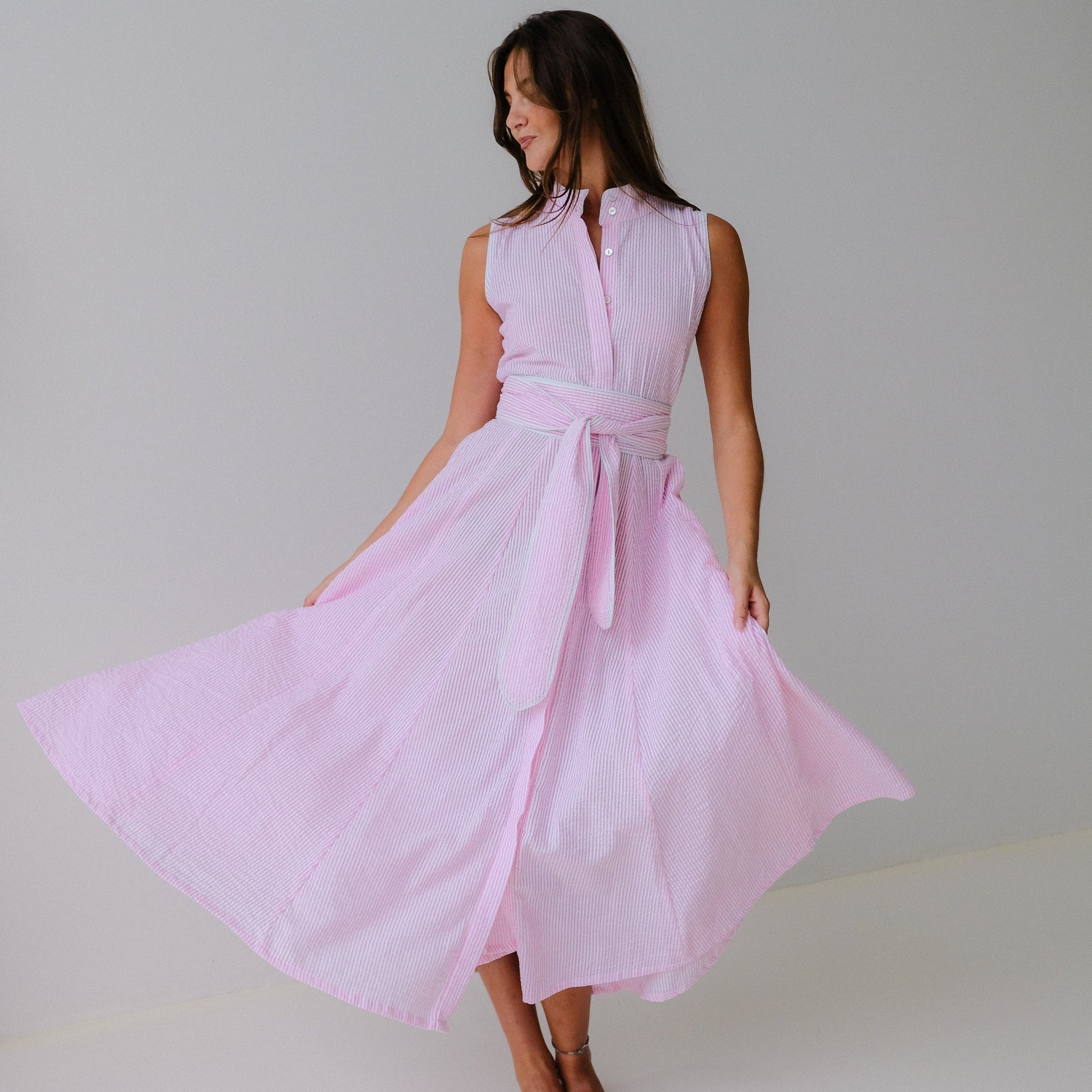 Woman wearing a light pink sleeveless dress with a belt against a plain background