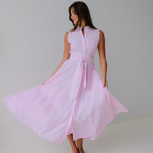 Woman wearing a light pink sleeveless dress with a belt against a plain background