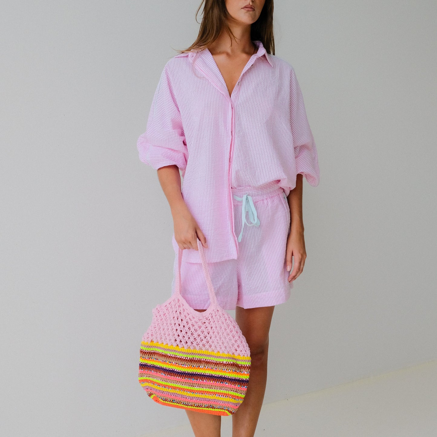 Woman in pink outfit holding a colorful bag against a plain background