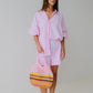 Woman in pink outfit holding a colorful bag against a plain background