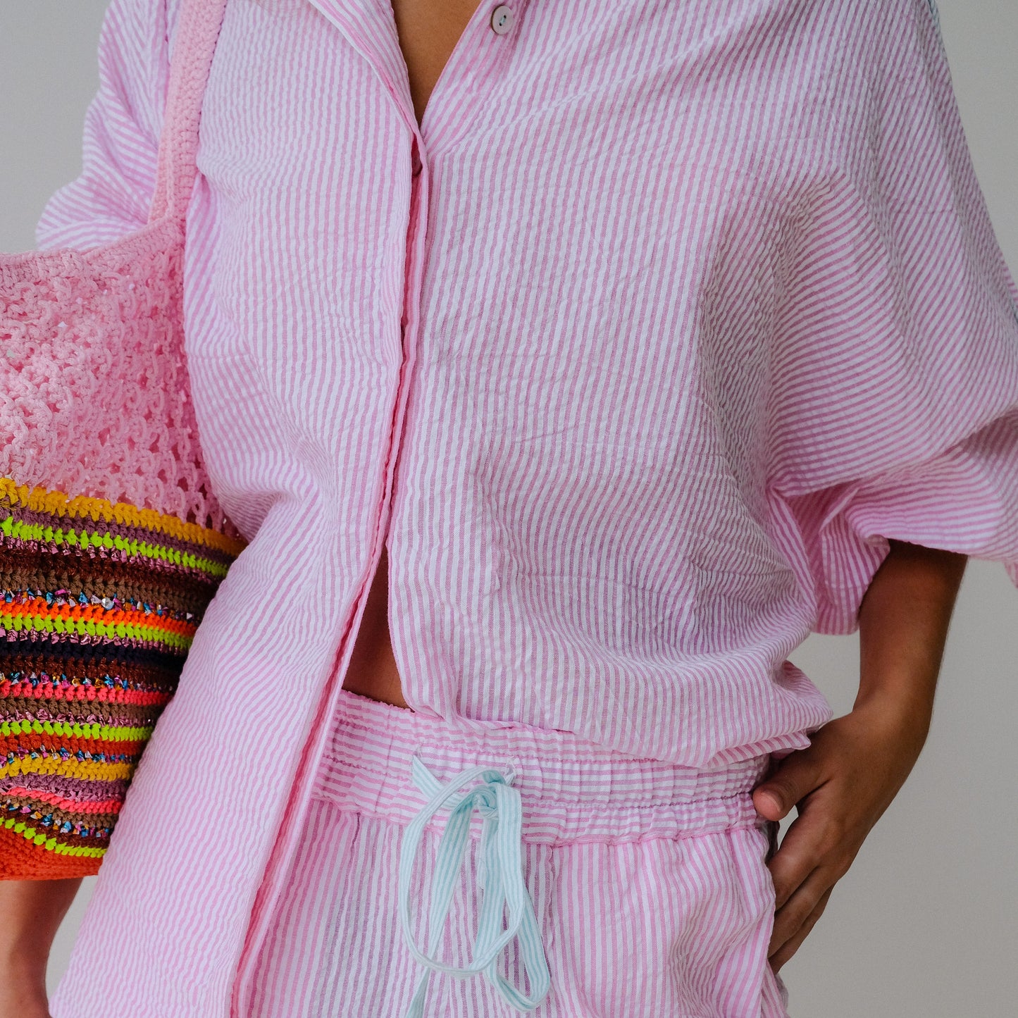 Person wearing a pink striped outfit with a colorful bag on a neutral background