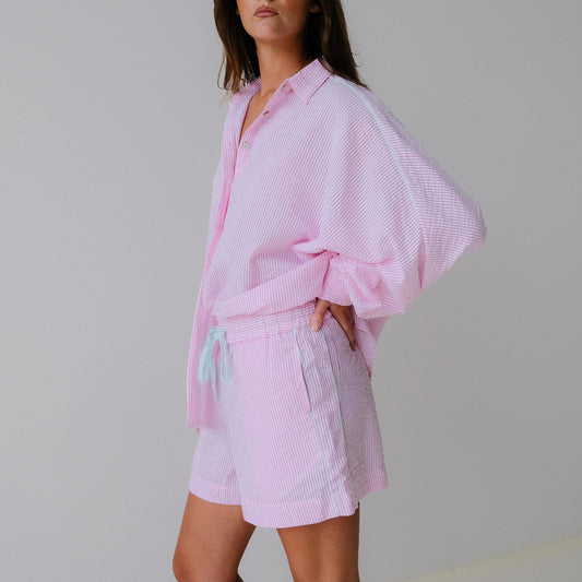 Woman wearing a light pink outfit with a matching jacket and shorts on a plain background