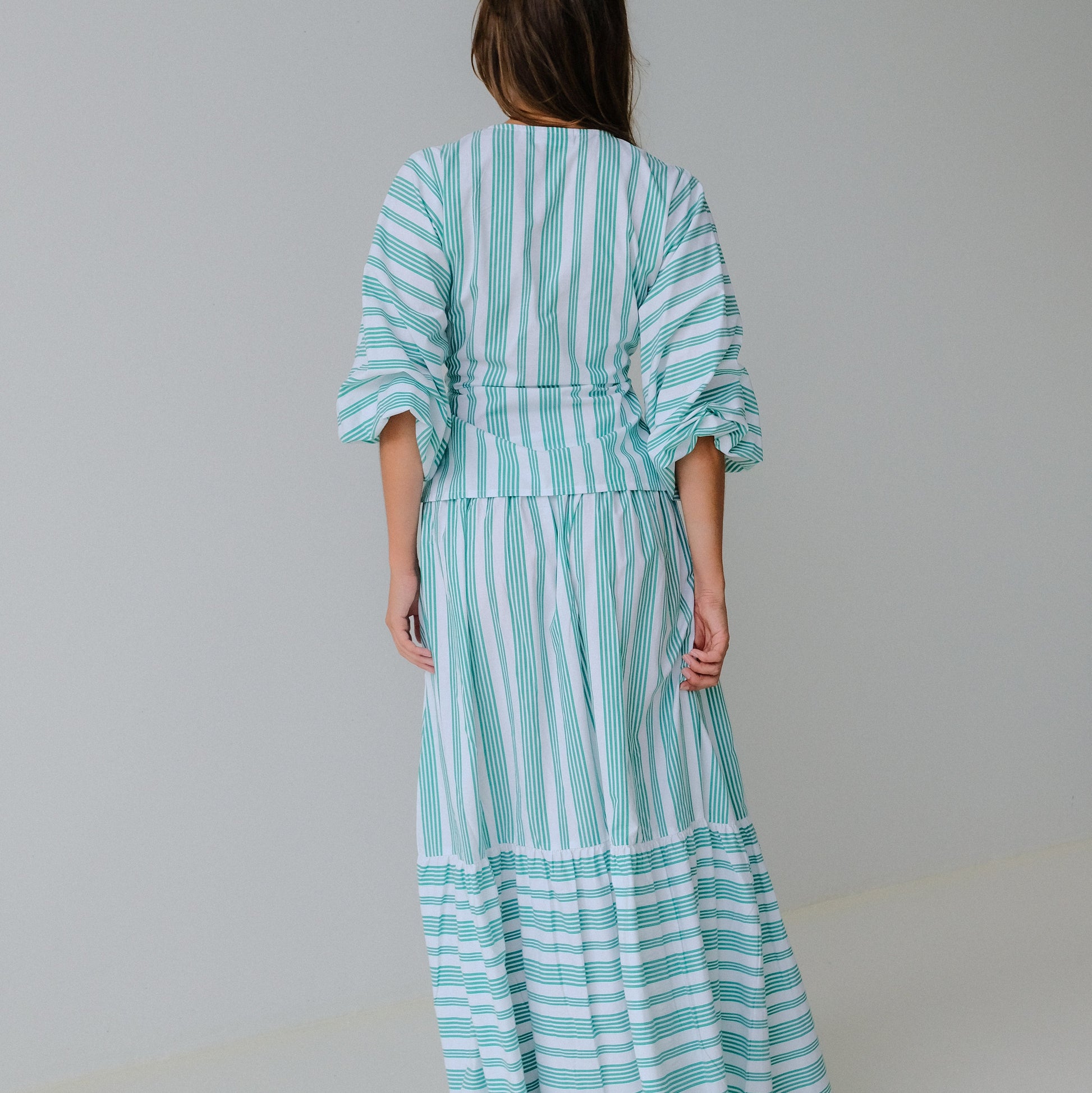 Woman wearing a turquoise and white striped dress against a plain background