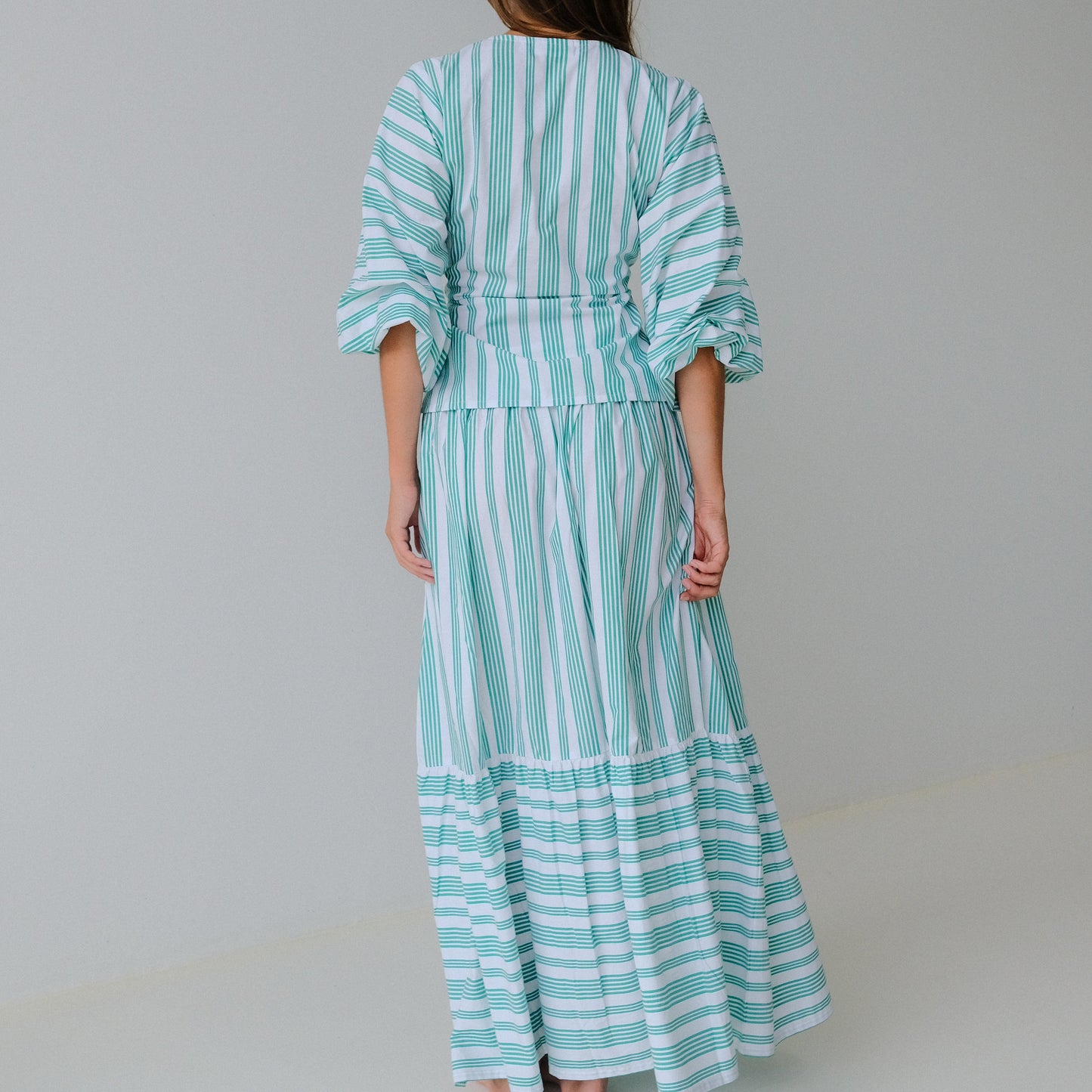Woman wearing a turquoise and white striped skirt & top against a plain background
