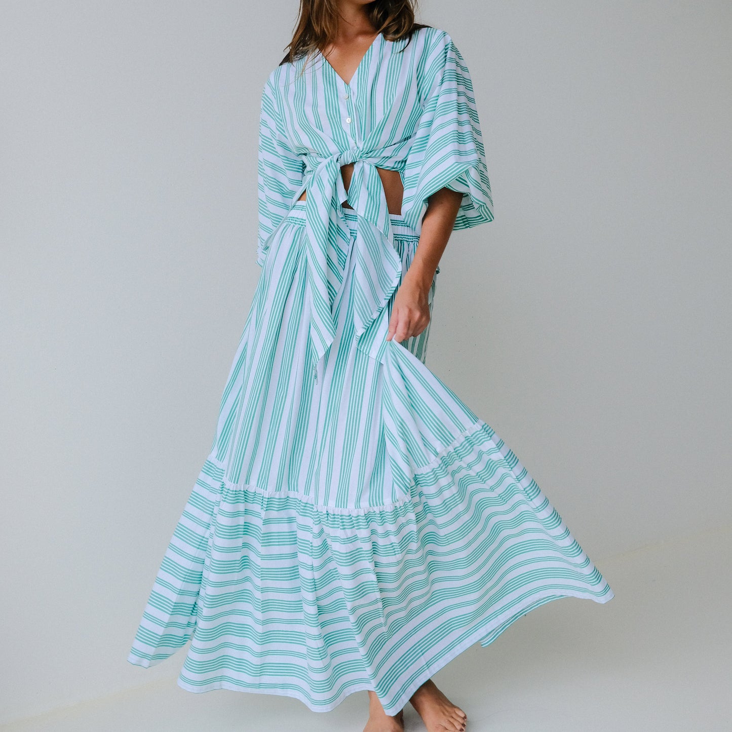 Woman wearing a long, light blue and white striped skirt & top on a plain background