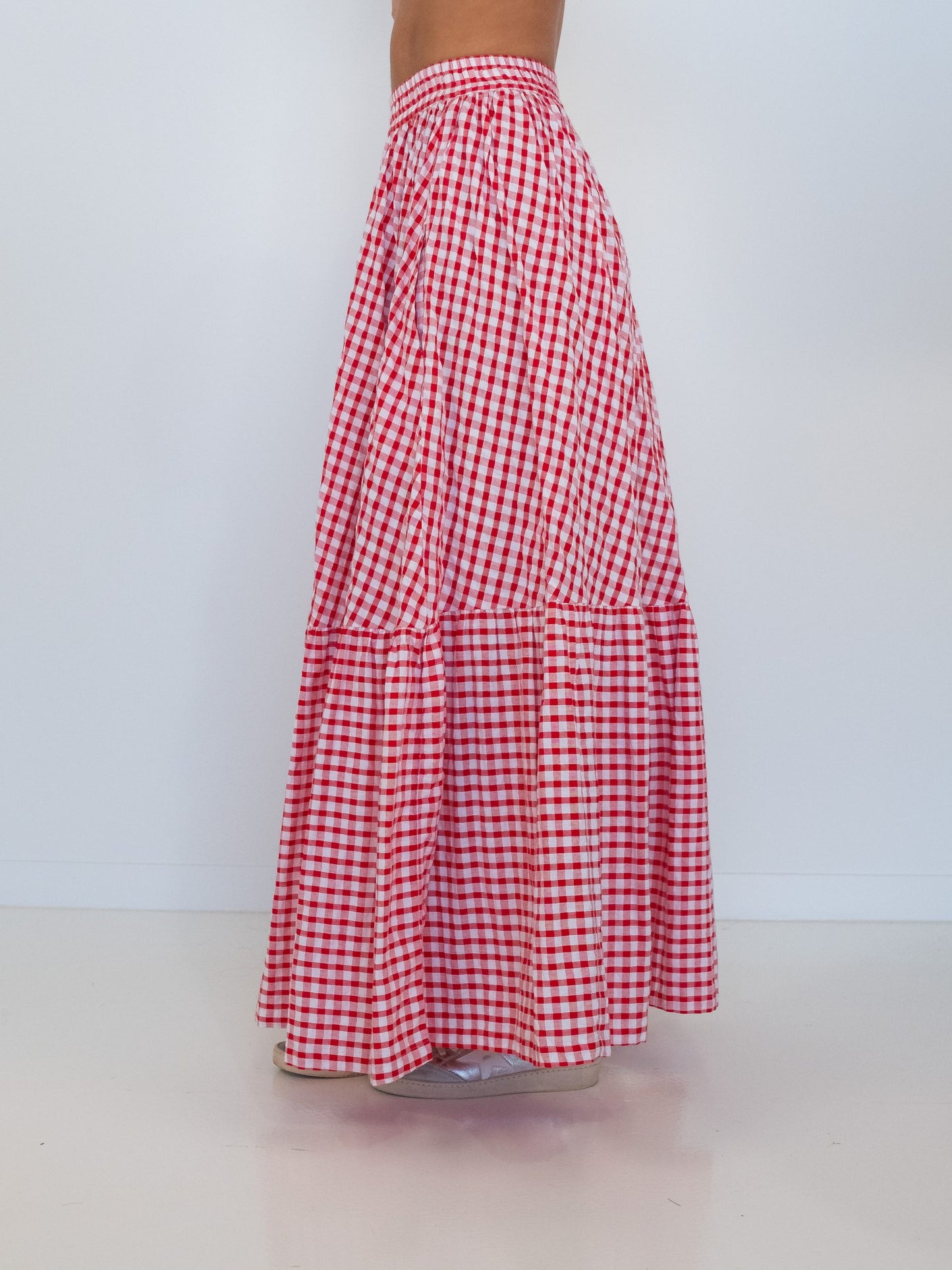 A red and white gingham tiered maxi skirt shown from the back on a model, featuring an elastic waistband and two ruffled tiers, set against a plain white studio background.