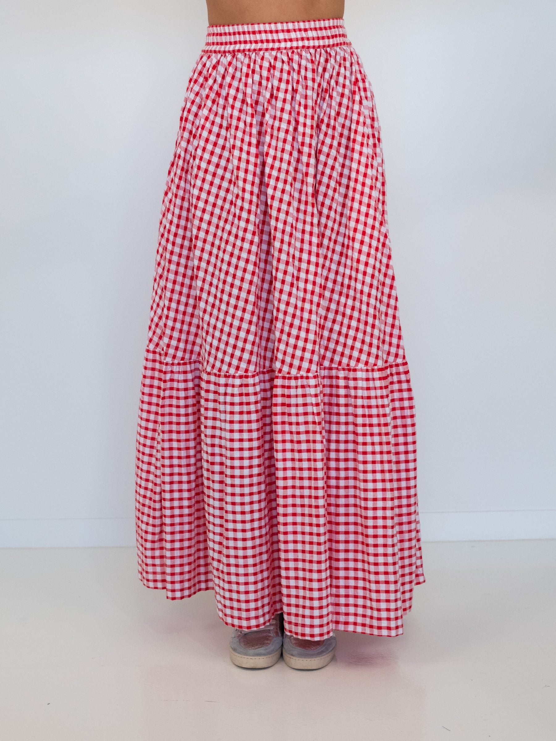 A red and white gingham tiered maxi skirt shown on a model from the waist down, featuring an elastic waistband and two gathered tiers, set against a plain white background.