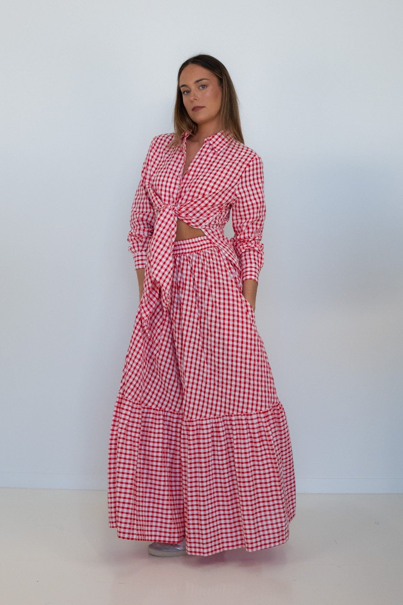 A red and white gingham tiered maxi dress with a wrap-style long-sleeve top and side pockets, shown on a model against a white background.