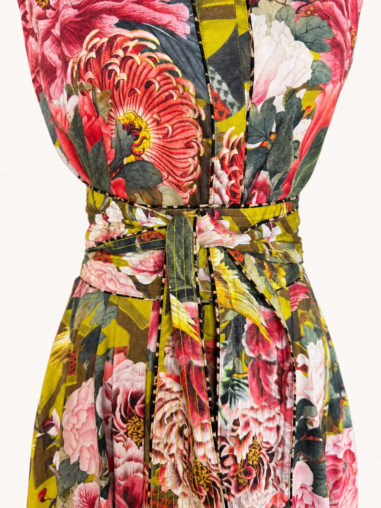 A close-up of a floral print dress with a matching tie belt, featuring a bold pattern of pink, red, yellow, and green flowers and leaves.