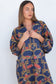 A woman wearing a loose, long-sleeve dress with a bold geometric pattern in navy blue, gold, and rust red, shown against a plain white background.
