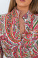 A close-up of a model wearing a long-sleeve button-up shirt with a vibrant red, green, and yellow paisley pattern on a white base.