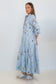 A woman modeling a light blue striped shirt dress with a colorful wildflower print, paired with silver sneakers, standing against a plain white studio background.